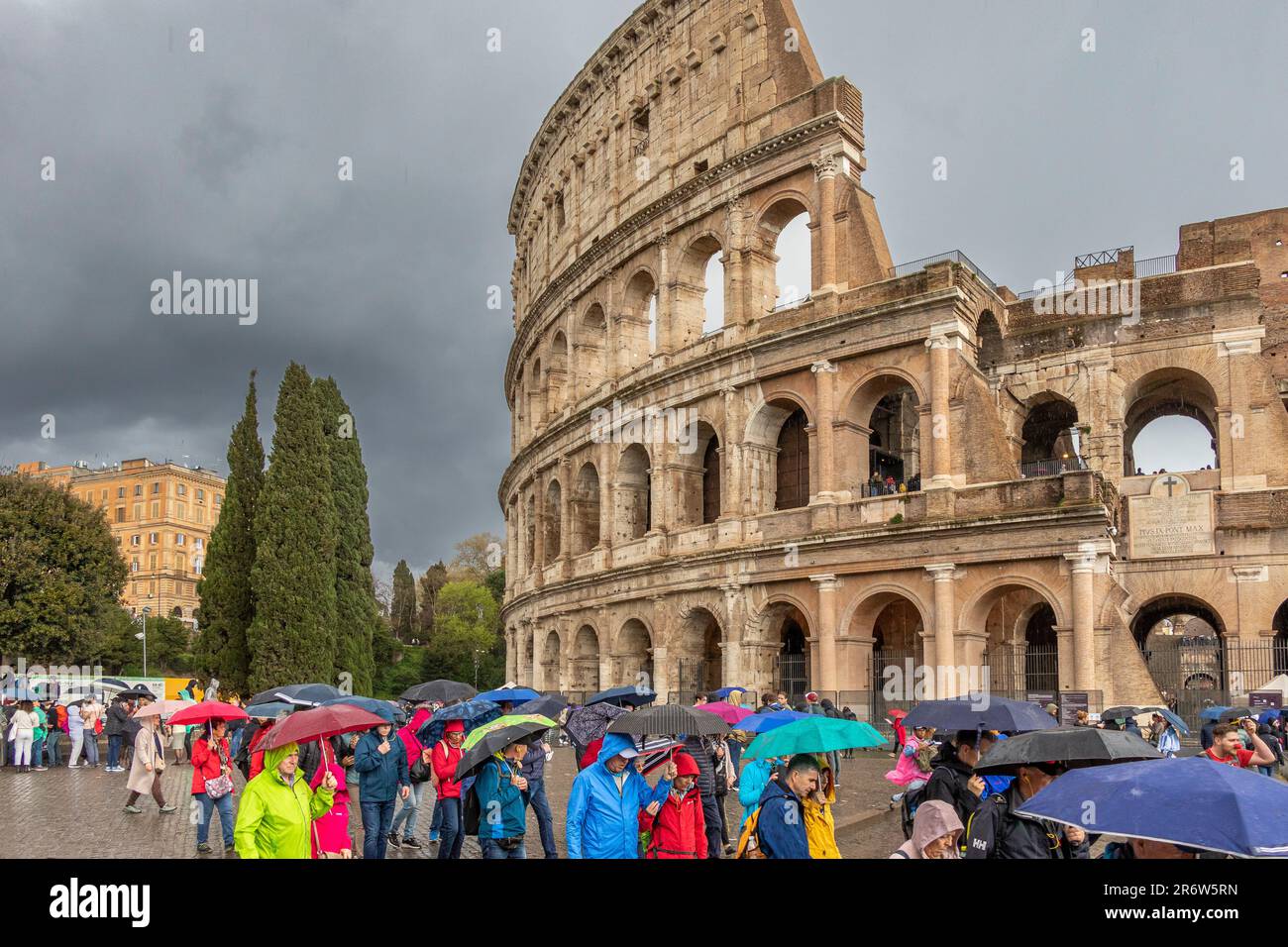 Persone con ombrelloni che visitano il Colosseo Romano durante le forti piogge e i cieli bui e tempestosi , Roma, Italia Foto Stock