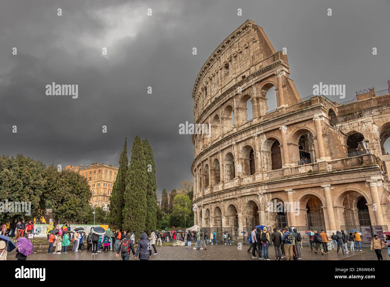 Persone con ombrelloni che visitano il Colosseo Romano durante le forti piogge e i cieli bui e tempestosi , Roma, Italia Foto Stock