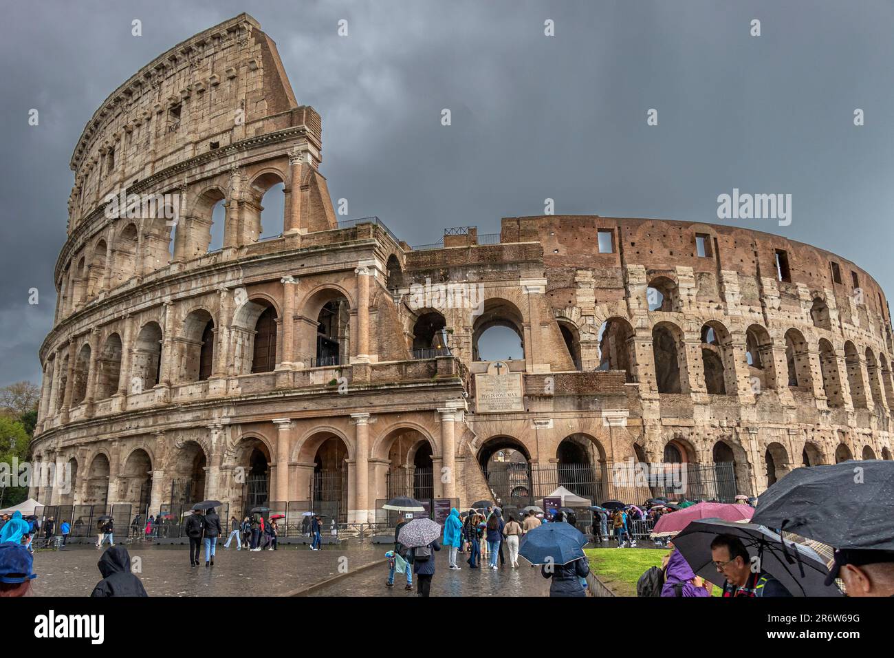 Persone con ombrelloni che visitano il Colosseo Romano durante le forti piogge e i cieli bui e tempestosi , Roma, Italia Foto Stock