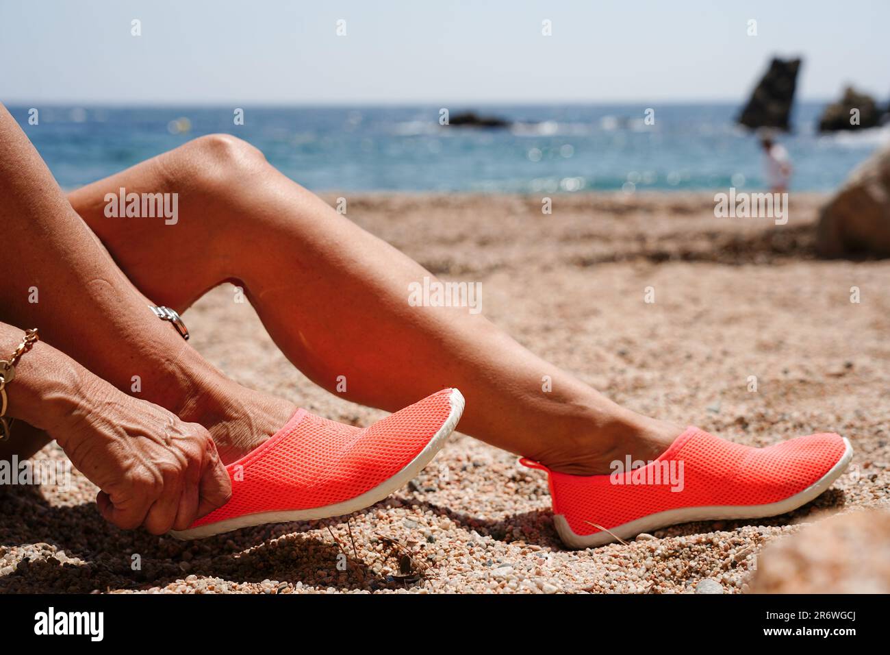 Due gambe con infradito arancione sulla spiaggia di sabbia nelle vacanze estive. Foto Stock