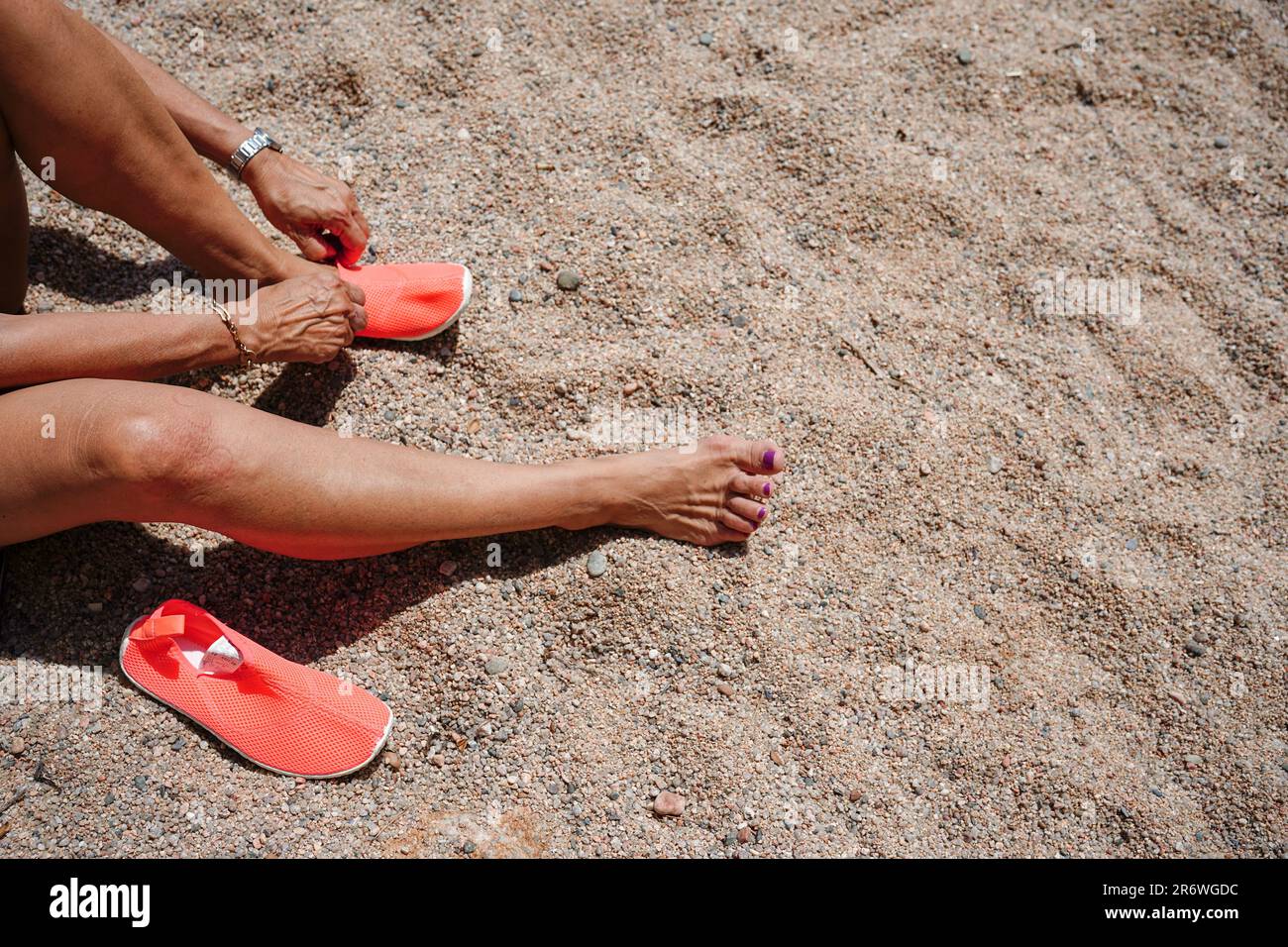 Due gambe con infradito arancione sulla spiaggia nella sabbia durante le vacanze estive. donna irriconoscibile Foto Stock