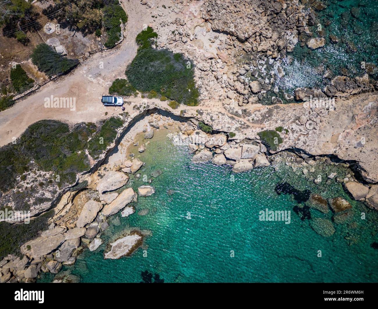 Vista aerea di un bianco off-roader in un viaggio su strada sulla costa della Grecia con turchese, acqua limpida e rocce Foto Stock