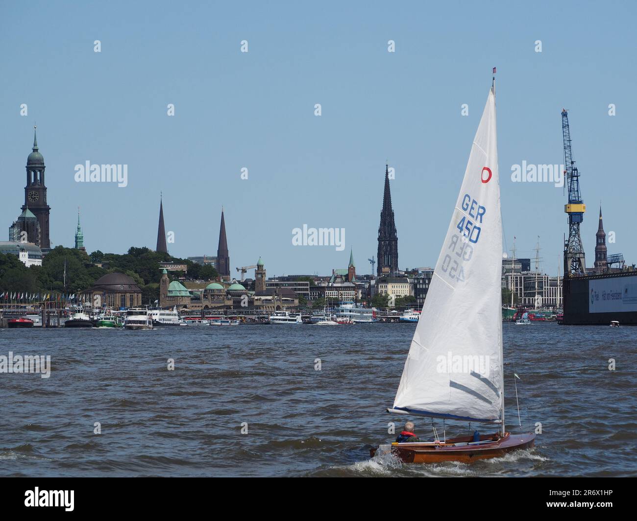 Uomo che naviga sulla sua classica barca a vela in legno nel porto di Amburgo, in Germania, con lo skyline del centro città sullo sfondo. Foto Stock