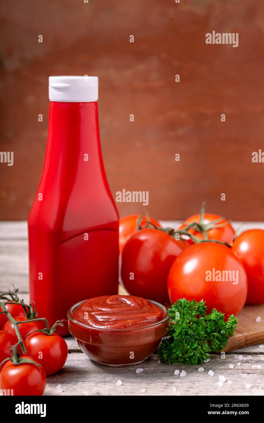 Bottiglia di plastica e ciotola di vetro di ketchup o salsa di pomodoro, spezie e pomodori freschi su tavola di legno. Messa a fuoco selettiva. Foto Stock