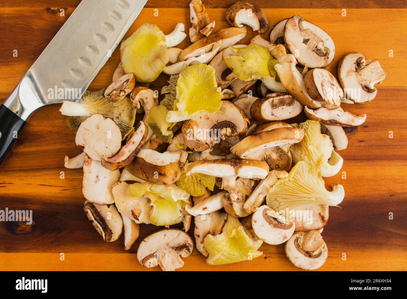 Funghi selvatici tagliati a fette con un coltello dello chef su un tagliere di legno: Ostriche preparate, shiitake e funghi porcini ammassati su un tagliere Foto Stock