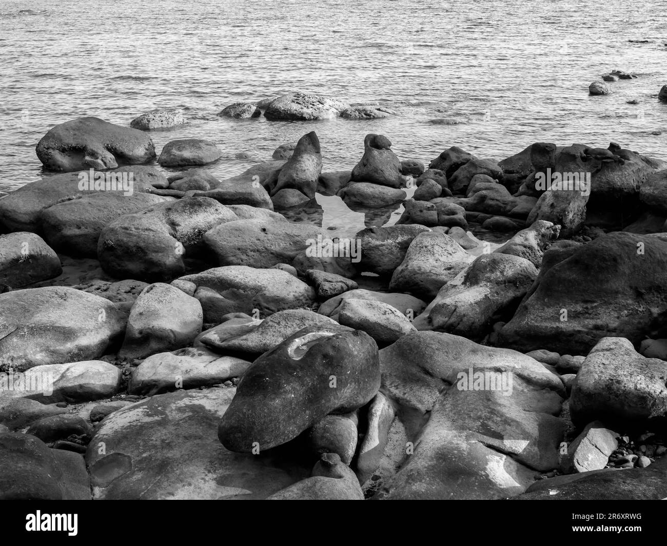 Splendida vista sul mare con rocce e acqua sullo sfondo dell'oceano, natura spettacolare. Bianco e nero del paesaggio della spiaggia con la costa rocciosa. Foto Stock