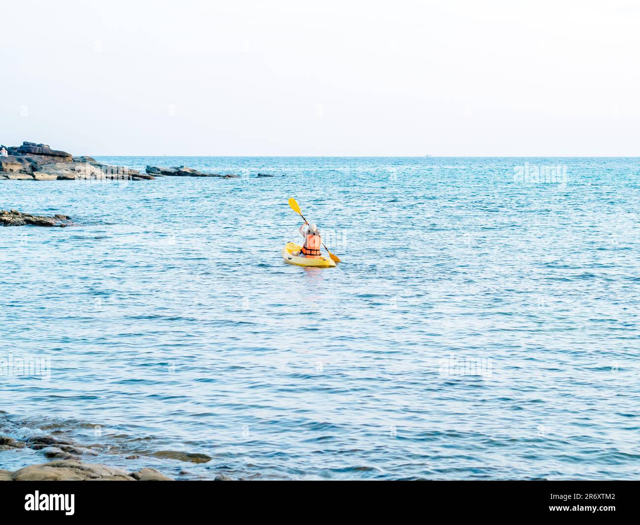 Dorso di donna asiatica in giubbotto salvagente e cappellino in kayak su una barca gialla in kayak con l'utilizzo di pagaia sul mare. Felice femmina che ha attività di divertimento sul mare vi Foto Stock