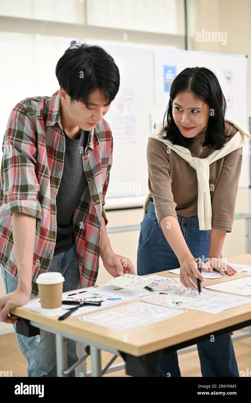 Un giovane e bello sviluppatore asiatico di siti web maschile sta parlando e pianificando un nuovo progetto con una collega in ufficio. UI, UX, Tech Star Foto Stock