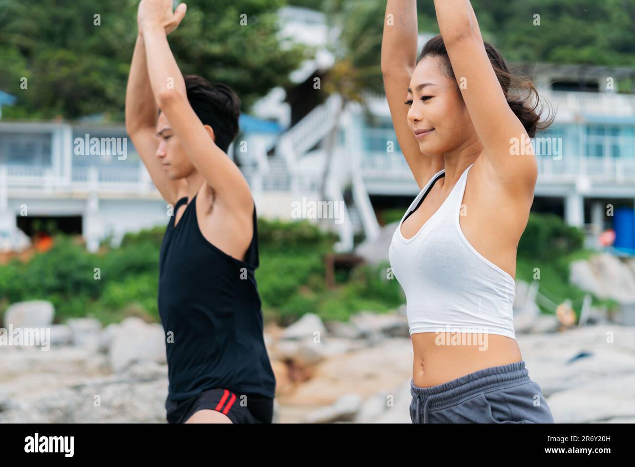 Pacifica e consapevole Asian 30s coppia godendo albero posa yoga sul mare. Coppia di uomini e donne sta addestrando la meditazione e la spiritualità Foto Stock