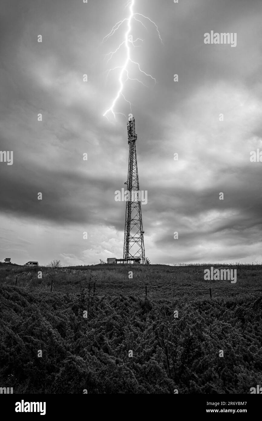 Fotografia in bianco e nero di una torre cellulare per telecomunicazioni con cielo nuvoloso e fulmine Foto Stock