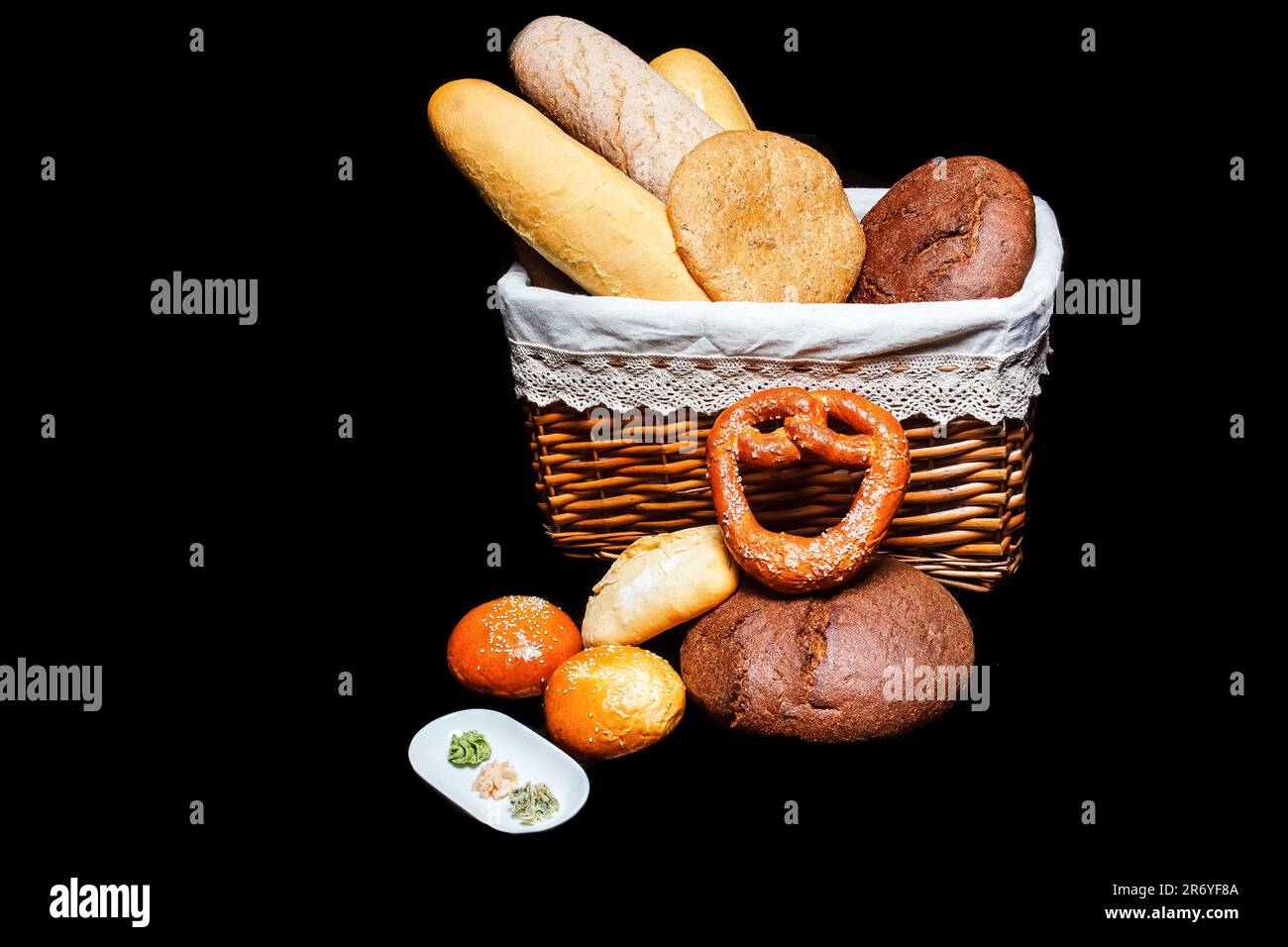 Un cesto di pane appena sfornato si distingue su uno sfondo nero, simboleggiando l'importanza di un'alimentazione sana e del benessere. Foto Stock