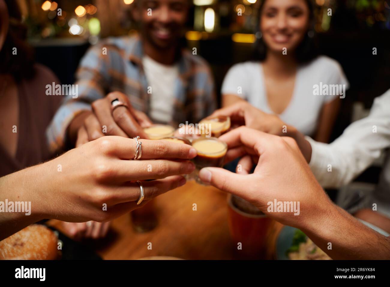 Primo piano di un giovane gruppo multirazziale di amici in abbigliamento casual brindisi con shot al ristorante Foto Stock