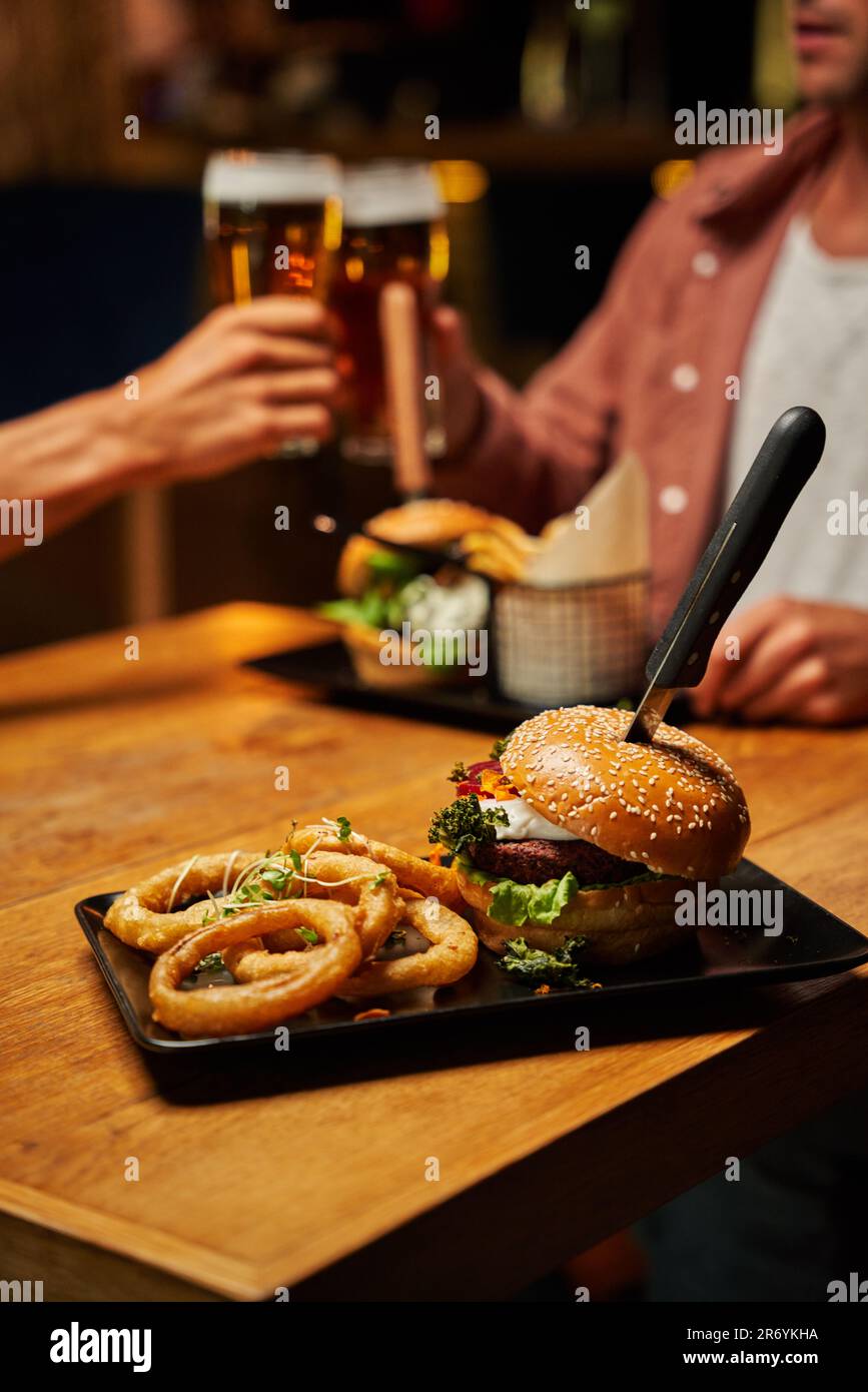 Primo piano di giovani coppie caucasiche in abbigliamento informale con fast food e birre al ristorante Foto Stock