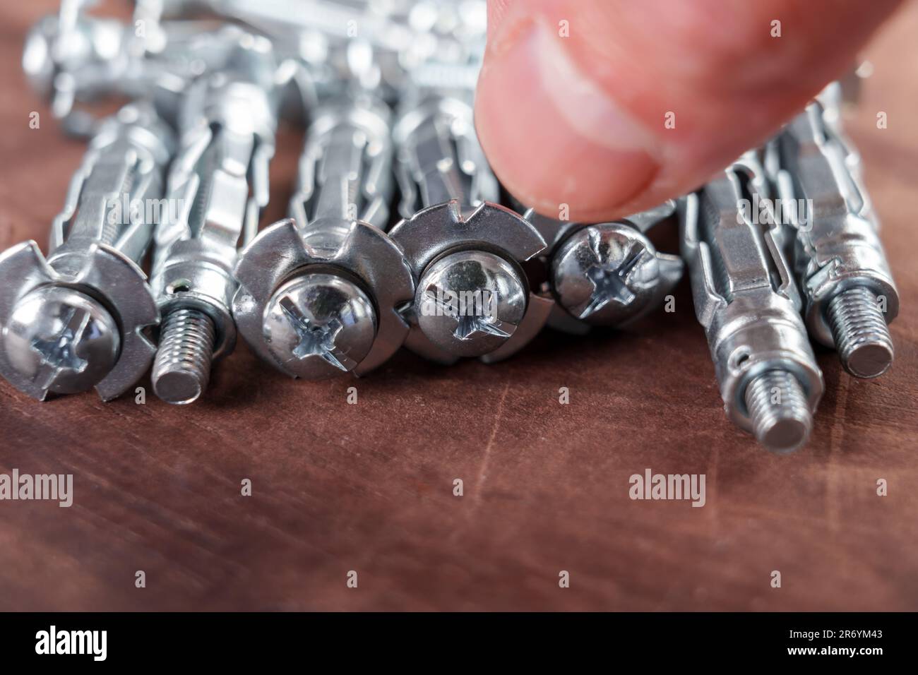 La mano prende il dispositivo di fissaggio per cartongesso molly Anchor. Primo piano su una tavola Foto Stock