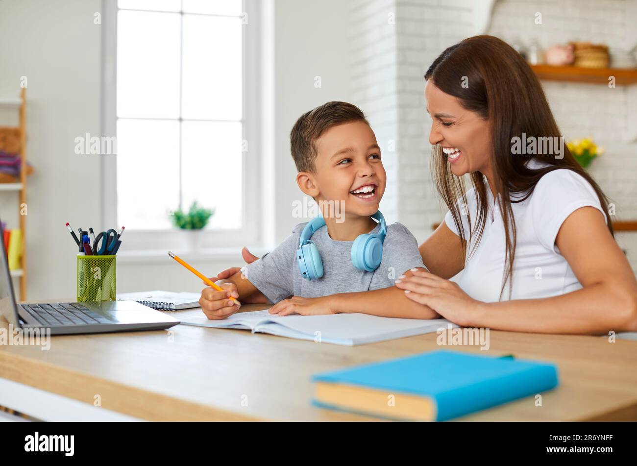 La giovane madre gioiosa a casa aiuta allegramente il suo figlio del primo grader a fare i suoi compiti. Foto Stock