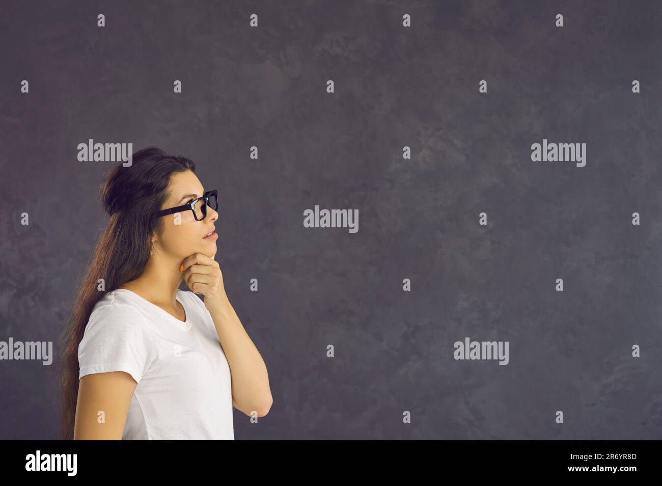 La giovane donna con un'espressione penitente si trova su uno sfondo grigio e pensa a qualcosa. Foto Stock