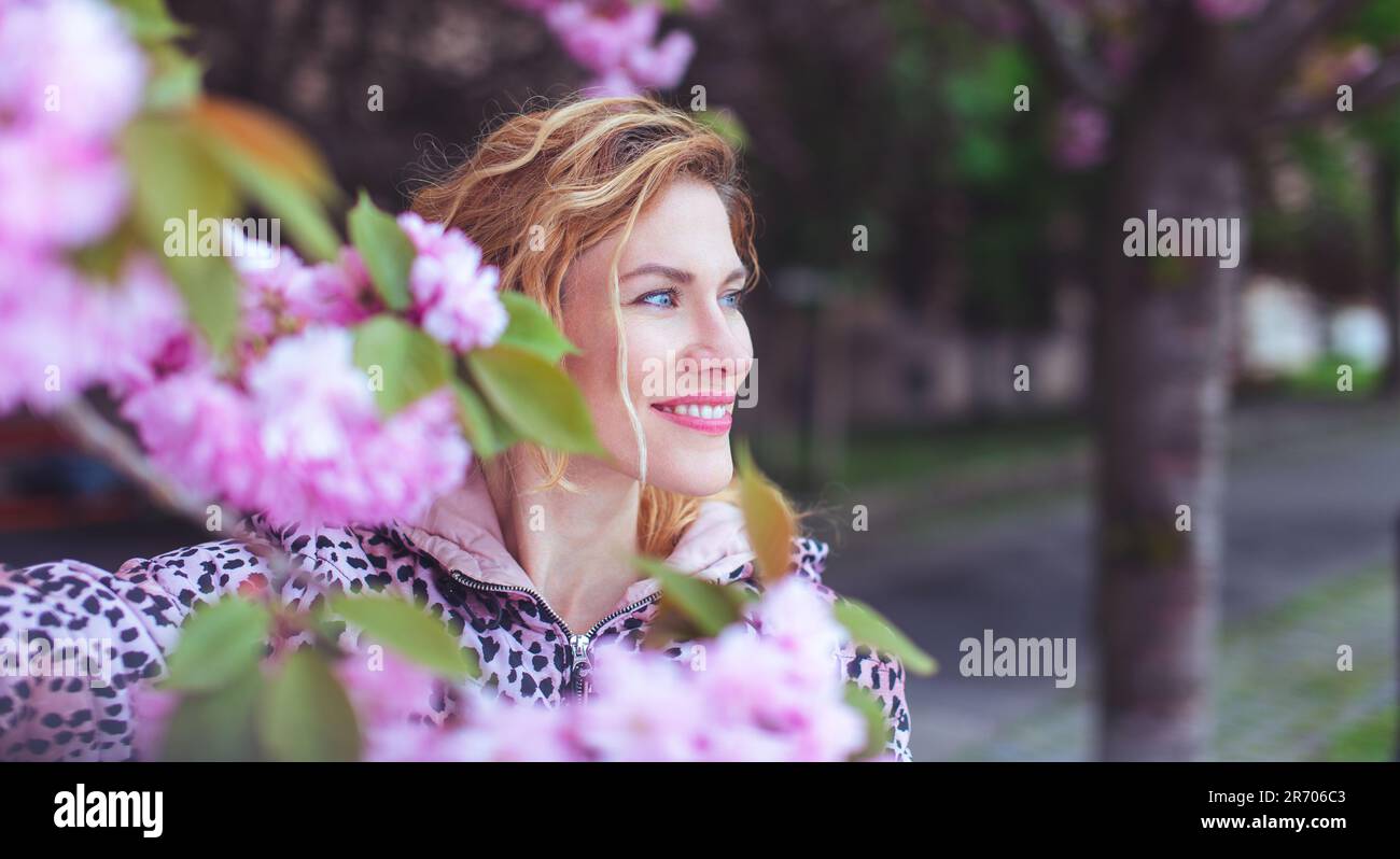 Donna felice guardando via nel parco durante la fioritura del ciliegio, Sakura Foto Stock