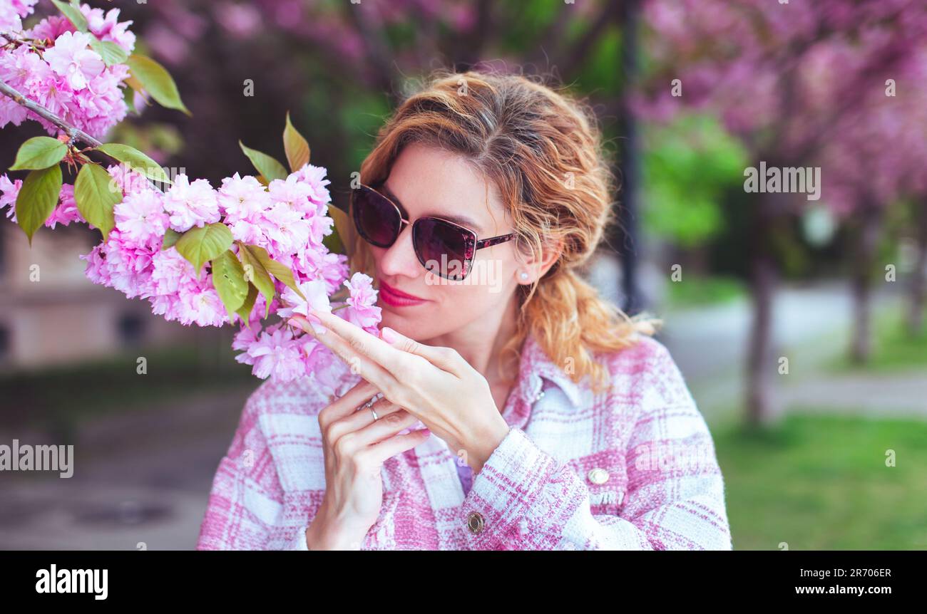 30s donna caucasica in occhiali da sole che odora la fioritura dei ciliegi Foto Stock