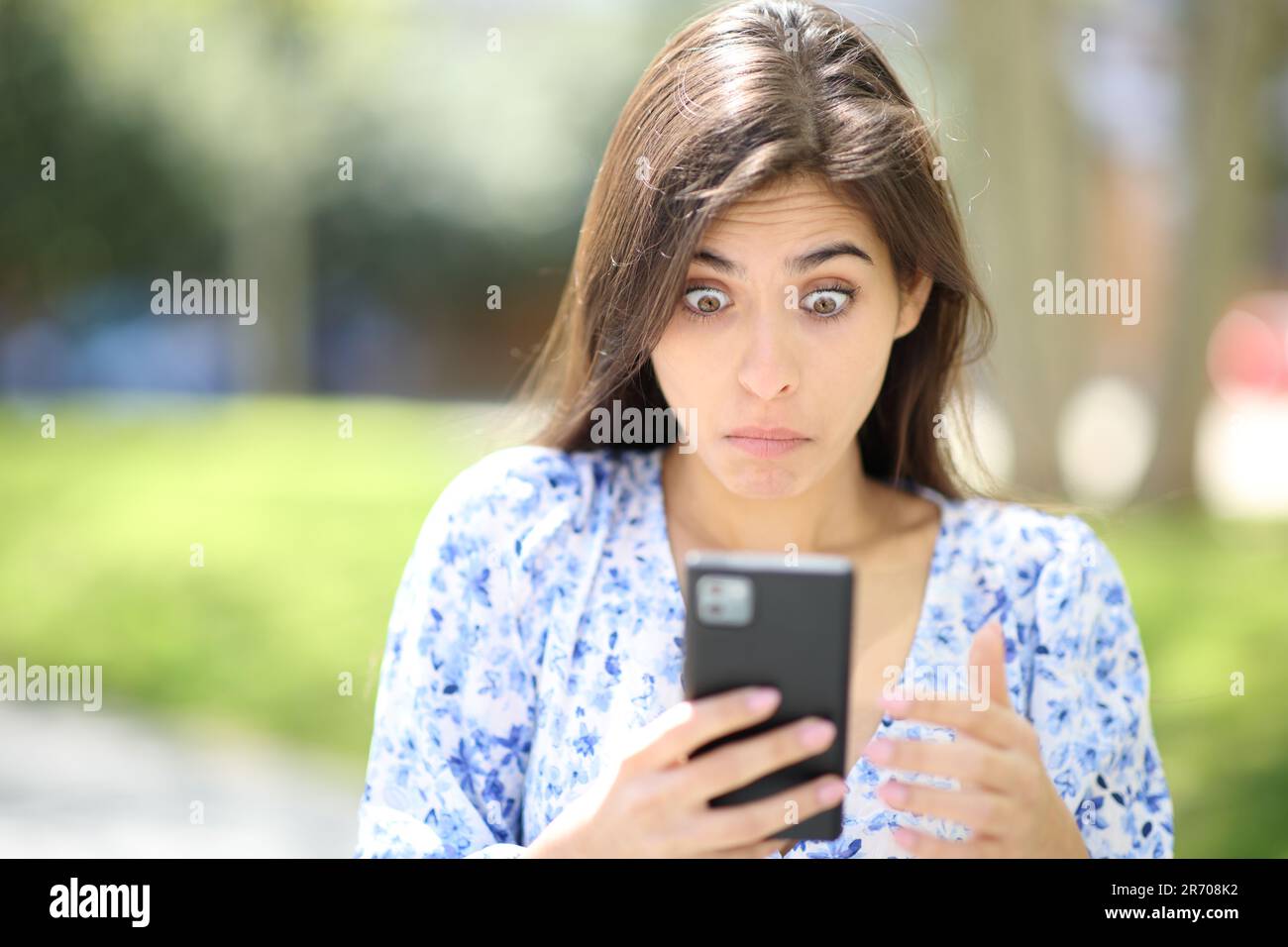Vista frontale di una donna perplessa che controlla il telefono in strada Foto Stock