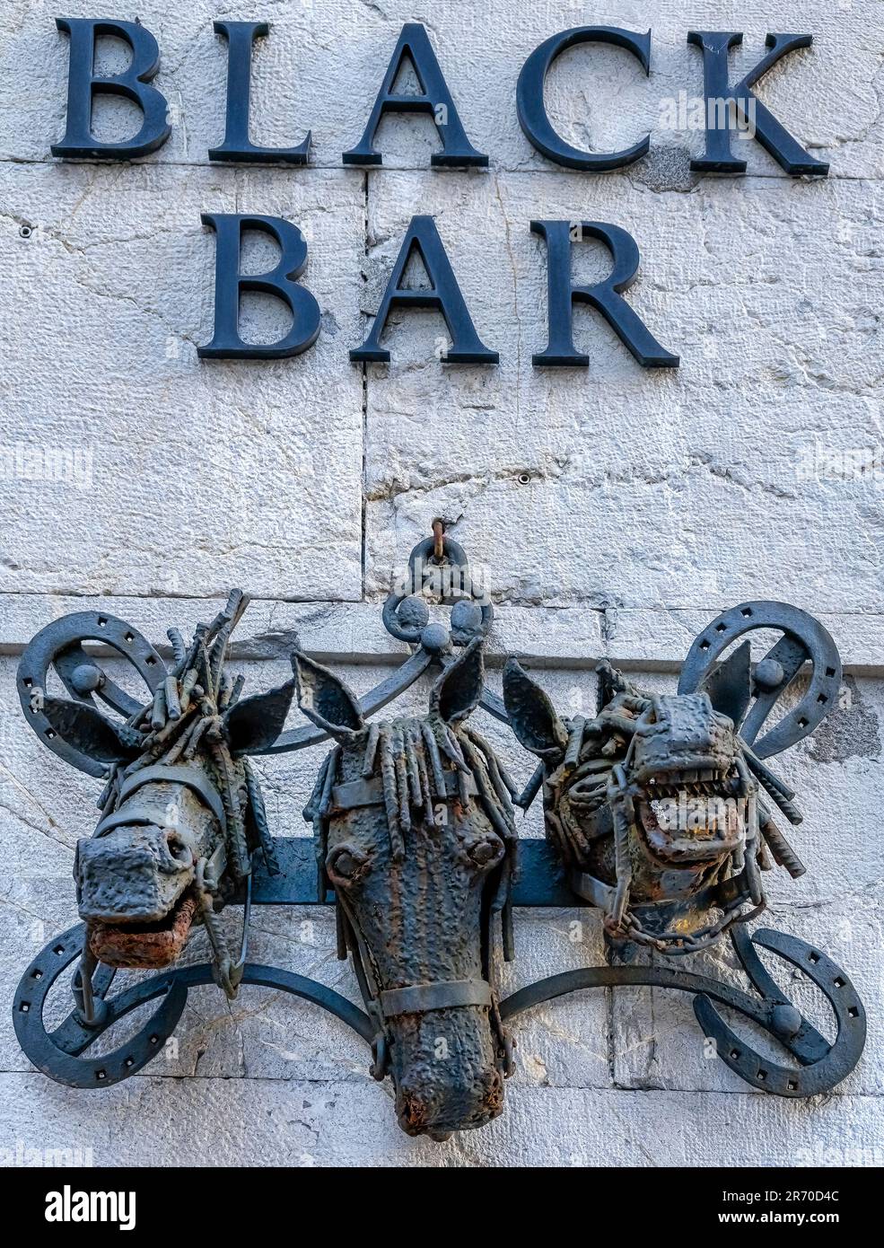 Oviedo, Asturias, Spagna: Un muro testurizzato con le parole Black Bar impresso su di esso. Una scultura di teste di cavallo di metallo è appesa ad un chiodo Foto Stock