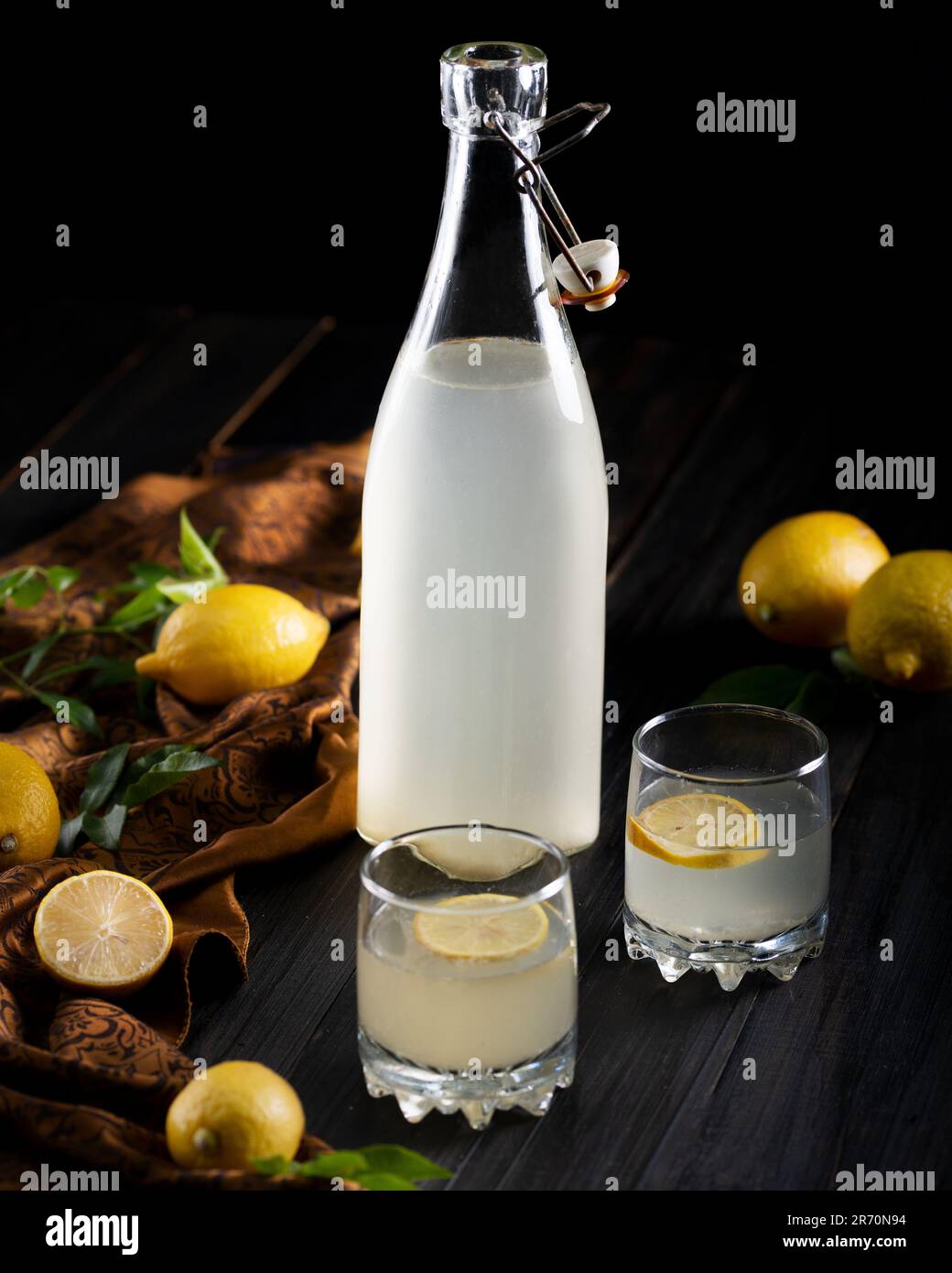 Un colpo verticale di una bottiglia di vetro riempita di limonata con limoni freschi su un tavolo Foto Stock