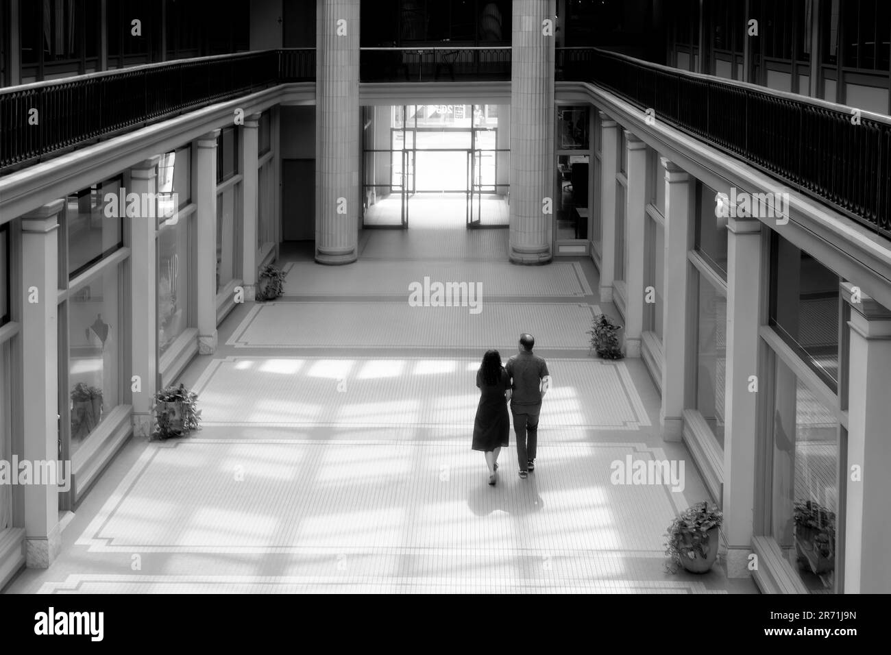 Coppia cammina attraverso la luce del sole che scorre in questo edificio arcade di metà secolo Foto Stock