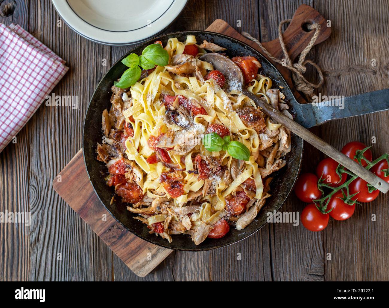 Pasta con carne di pollo arrosto, pomodori, cipolle, aglio ed erbe in una padella su tavola di legno Foto Stock