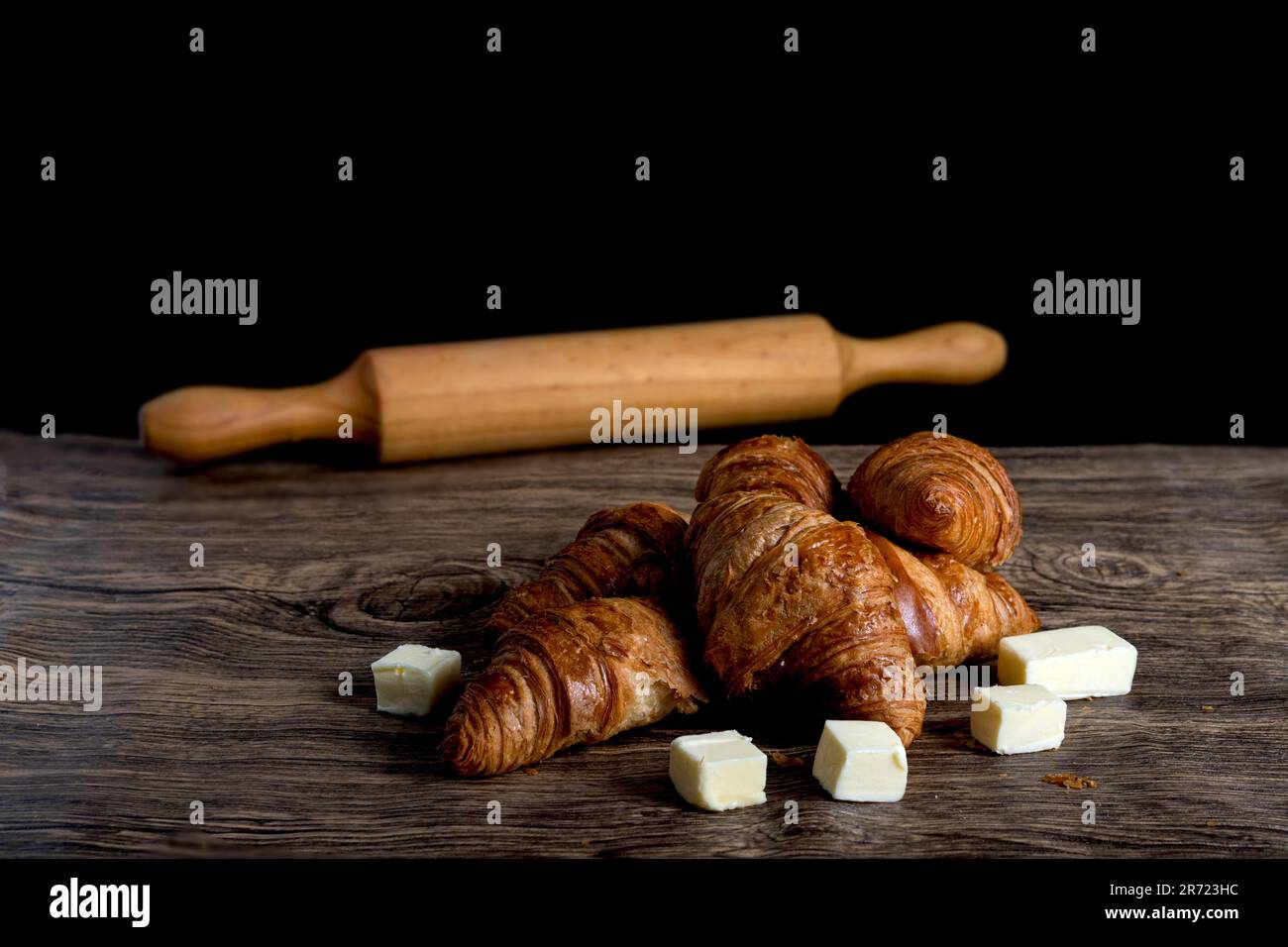 croissant con pezzi di burro e mattonelle su fondo nero e legno Foto Stock