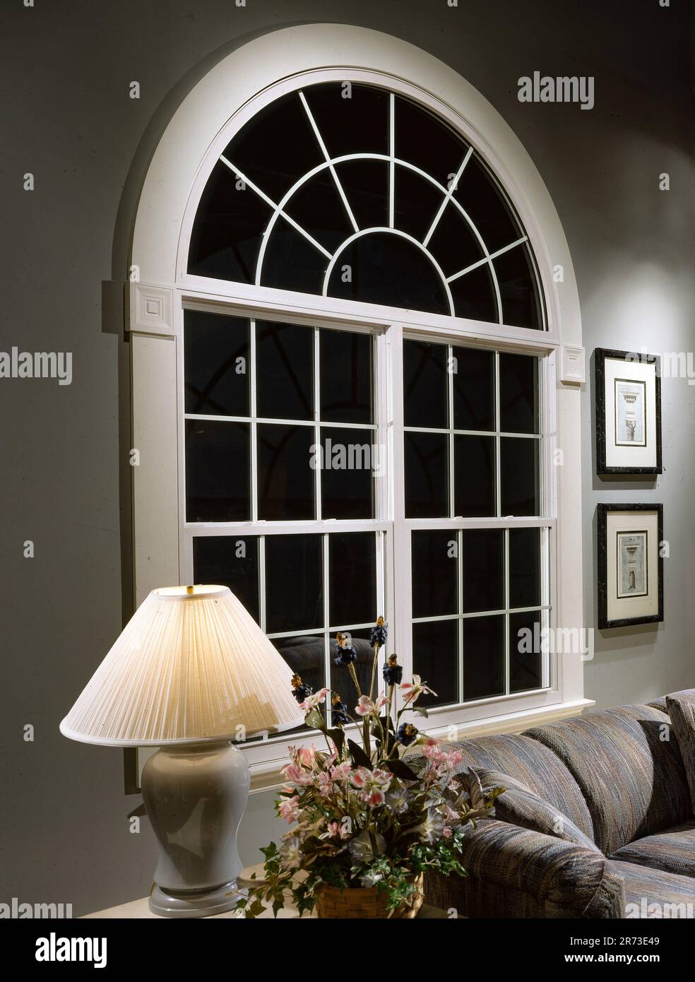 Elegante finestra ad arco con decorazioni in un soggiorno residenziale di notte, con illuminazione soffusa, divani e interni classici Foto Stock
