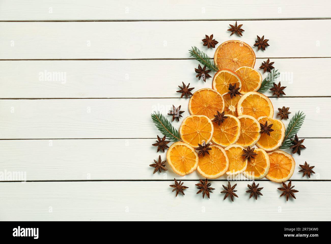 Composizione di posa piatta con fettine di arancio secco, rami di abete e stelle di anice disposte a forma di albero di Natale su tavola di legno bianco. Spazio per il testo Foto Stock