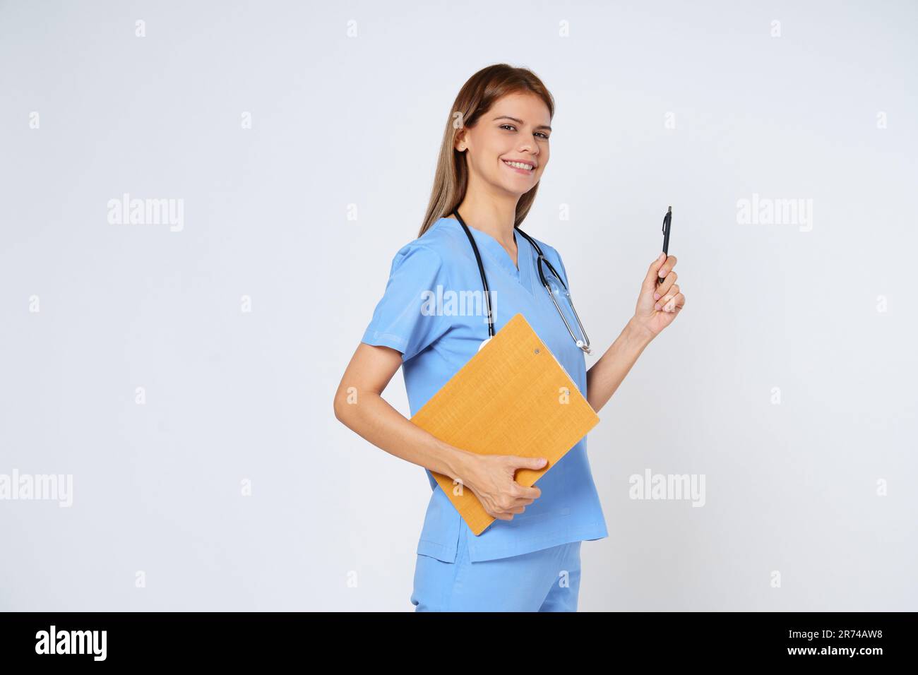 Donna sorridente medico alzando la penna e tenendo la clipboard, in piedi in uniforme isolato su sfondo bianco. Foto Stock