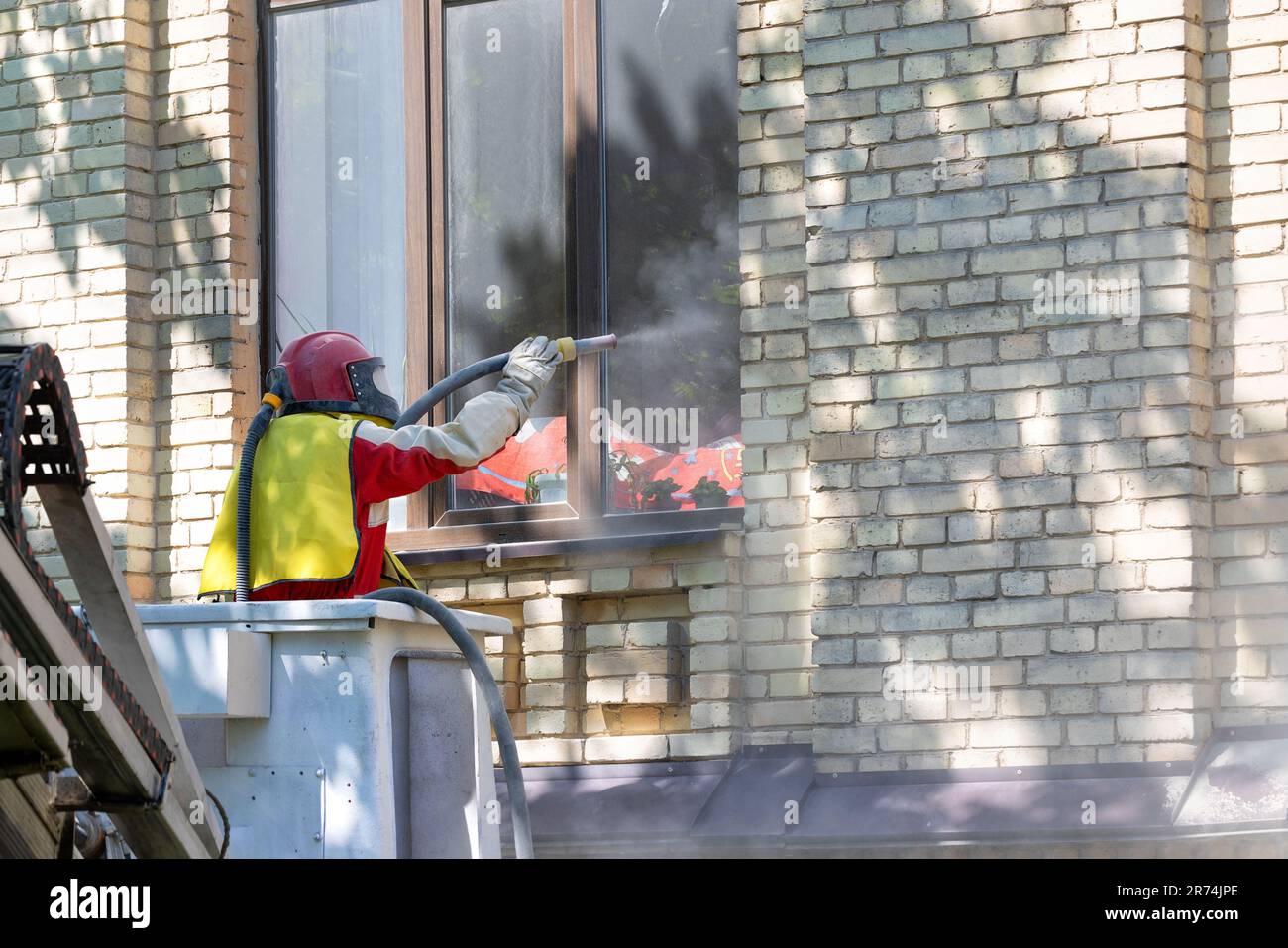 Un lavoratore in un vestito spazio protettivo pulisce la facciata di una vecchia casa di mattoni utilizzando un sabbiatore industriale. Foto Stock