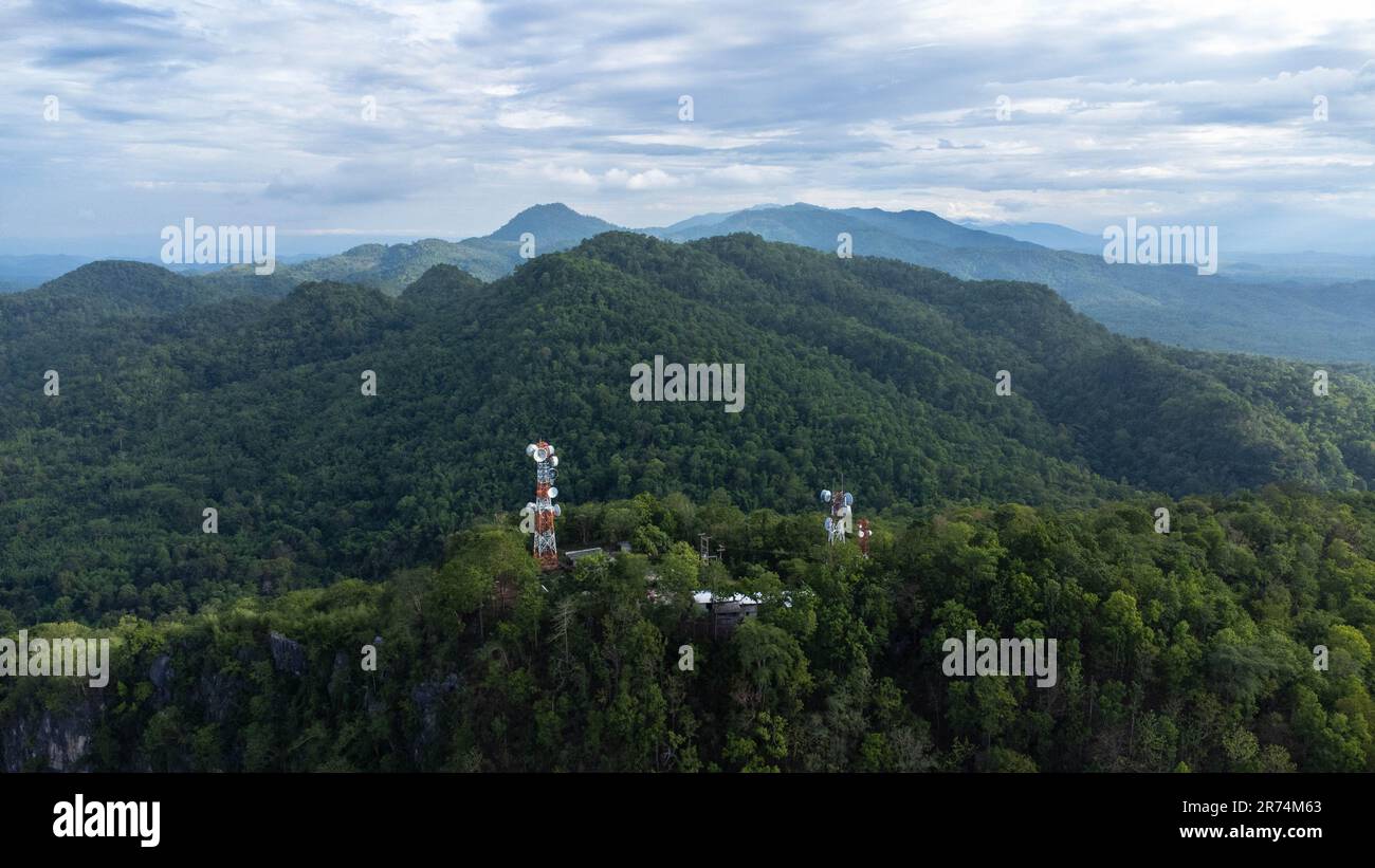 Torre di comunicazione, torre radio, torre di telecomunicazione o torre di trasmissione nella foresta sulla montagna con nuvole e cielo blu sfondo. Foto Stock