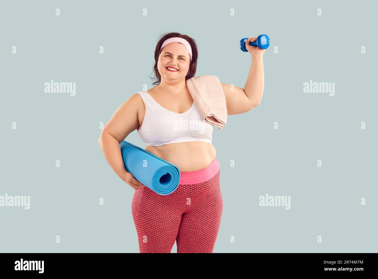 Ritratto di giovane donna felice in sovrappeso con manubri e tappetino fitness Foto Stock
