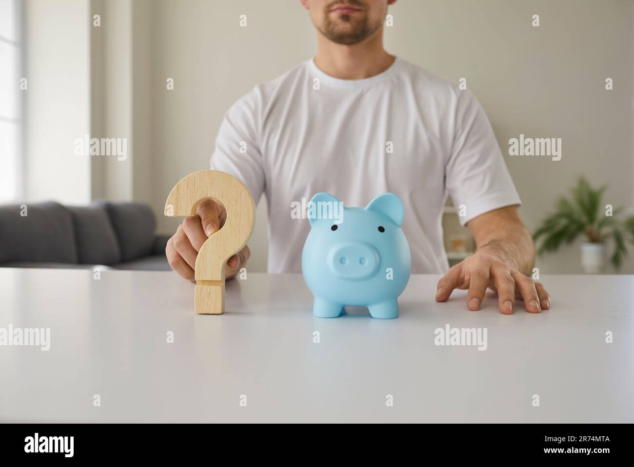 Uomo a tavola con una banca piggy e un punto interrogativo che mostrano il concetto di incertezza finanziaria Foto Stock