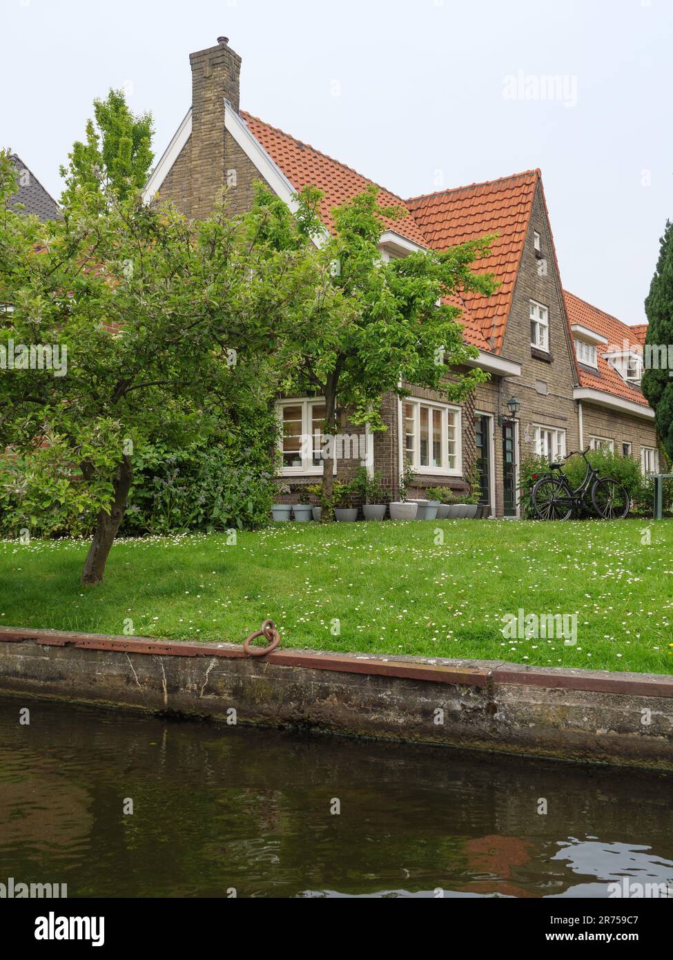 Una tradizionale casa costiera con tetti di tegole rosse e una piccola barca di legno ormeggiata accanto ad essa, situata su una tranquilla spiaggia che si affaccia sull'oceano Foto Stock