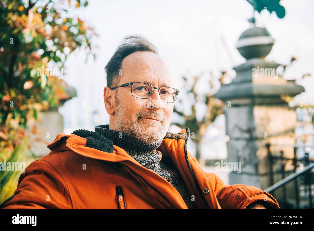 Ritratto all'aperto di un uomo di mezza età che indossa occhiali e giacca invernale arancione Foto Stock