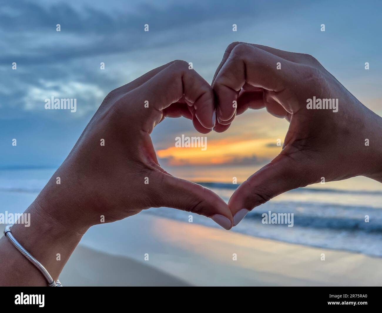 Nord America, Caraibi, grandi Antille, Isola di Hispaniola, Repubblica Dominicana, Provincia di Sama, Penisola di Sama, Playa Cosón, donna che forma un cuore con le mani davanti al tramonto sulla spiaggia di Playa Cosón Foto Stock