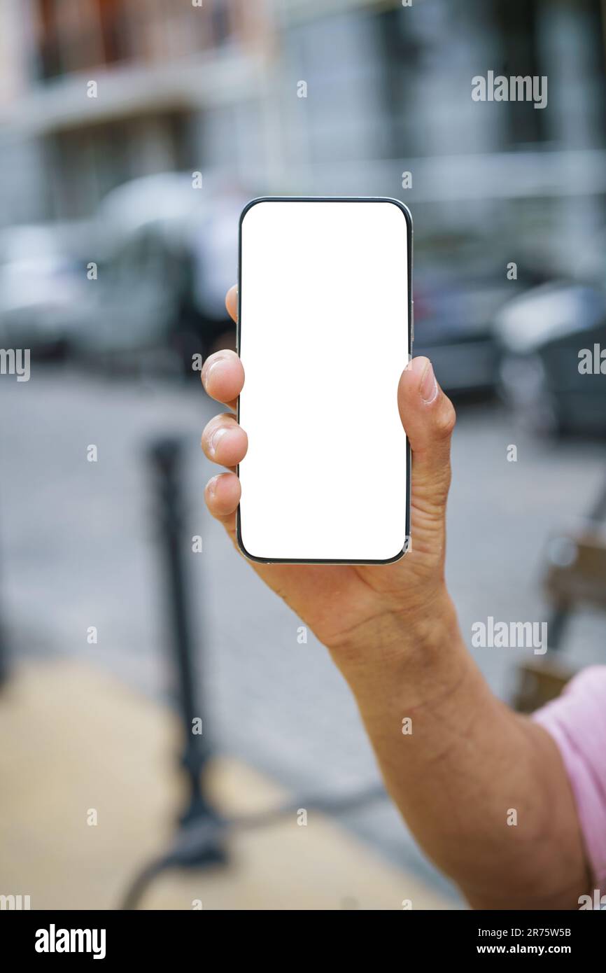 Primo piano del telefono cellulare con mano dell'uomo e display a schermo bianco, che offre un ampio spazio di copia. Lo sfondo presenta un paesaggio urbano che fornisce uno sfondo moderno e vibrante. . Foto di alta qualità Foto Stock