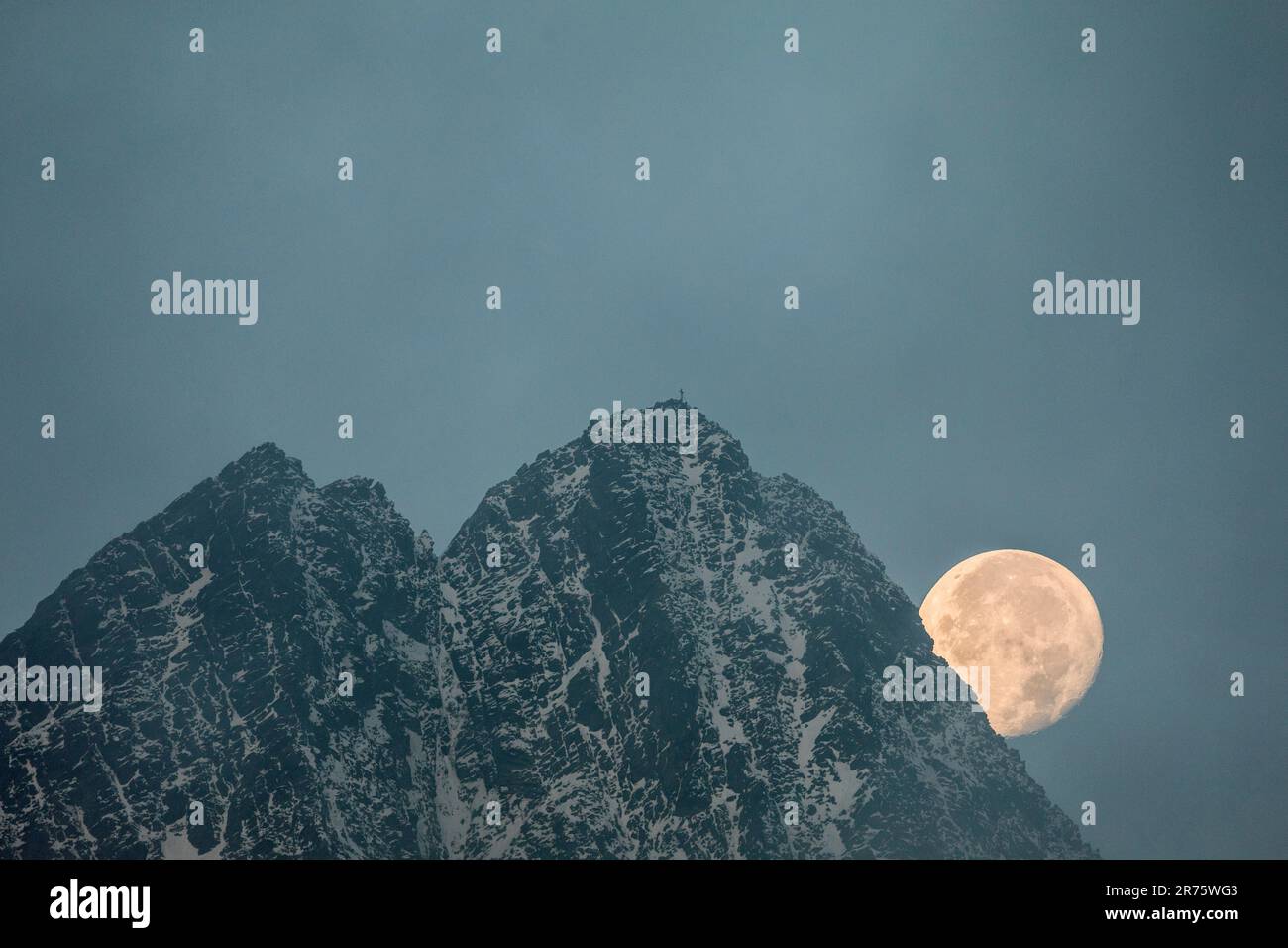 La luna piena scende accanto alla cima di Großglockner, alla nebbia, alla croce sommitale Foto Stock