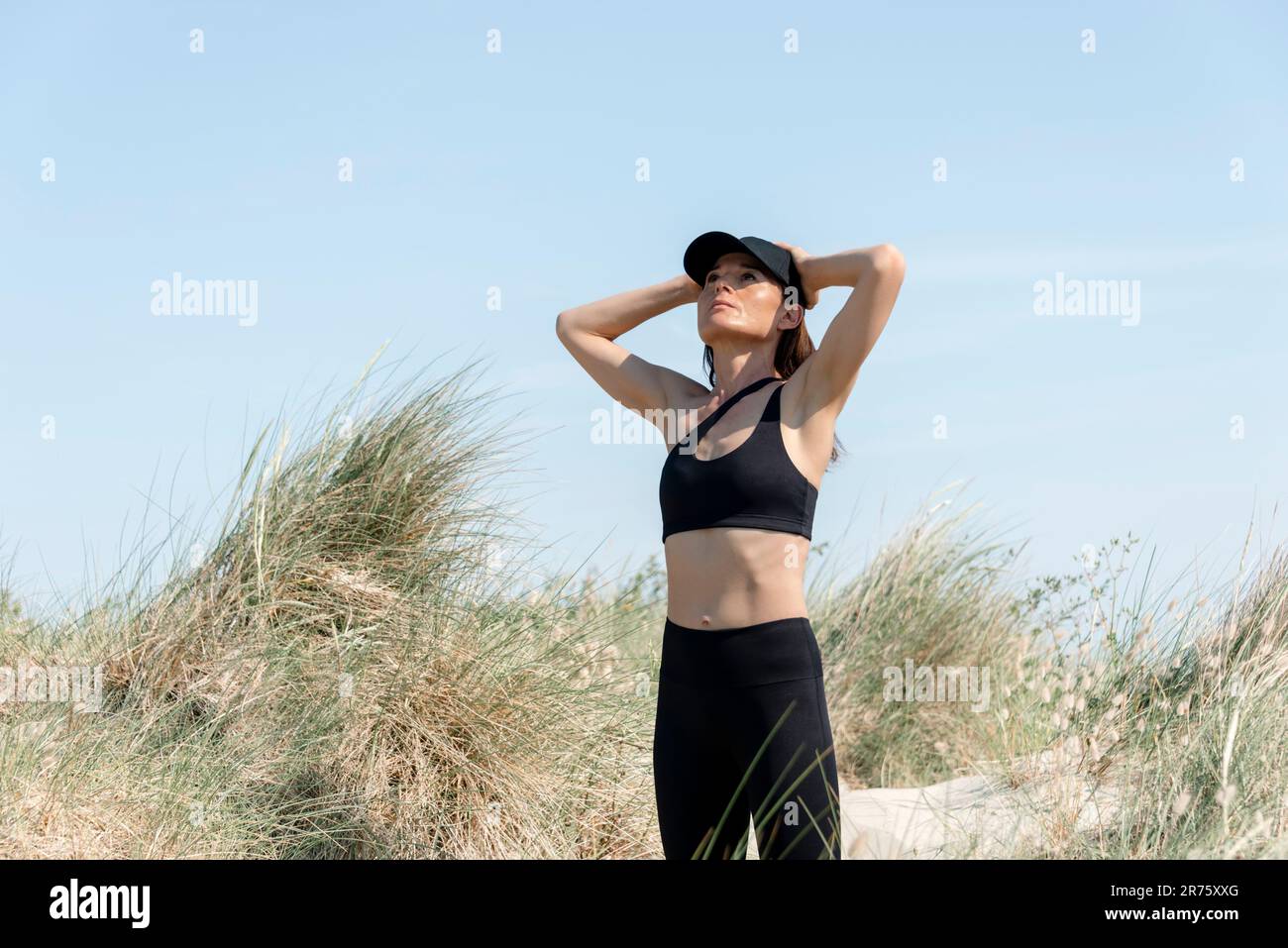Atleta sportiva nelle dune di sabbia con le mani sulla testa Foto Stock