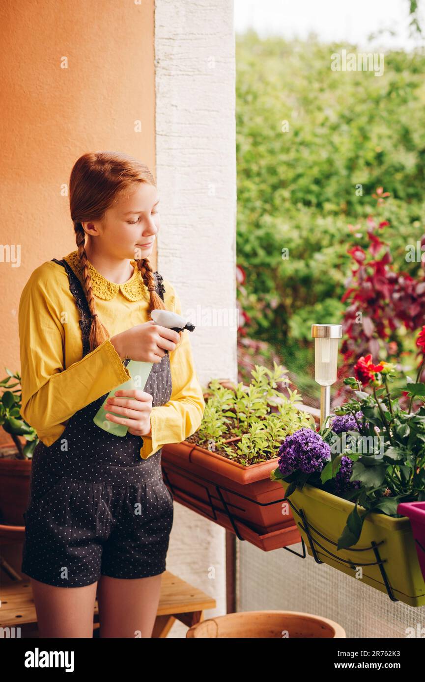 Adorabile bambina che innaffia le piante sul balcone in una bella giornata di sole Foto Stock