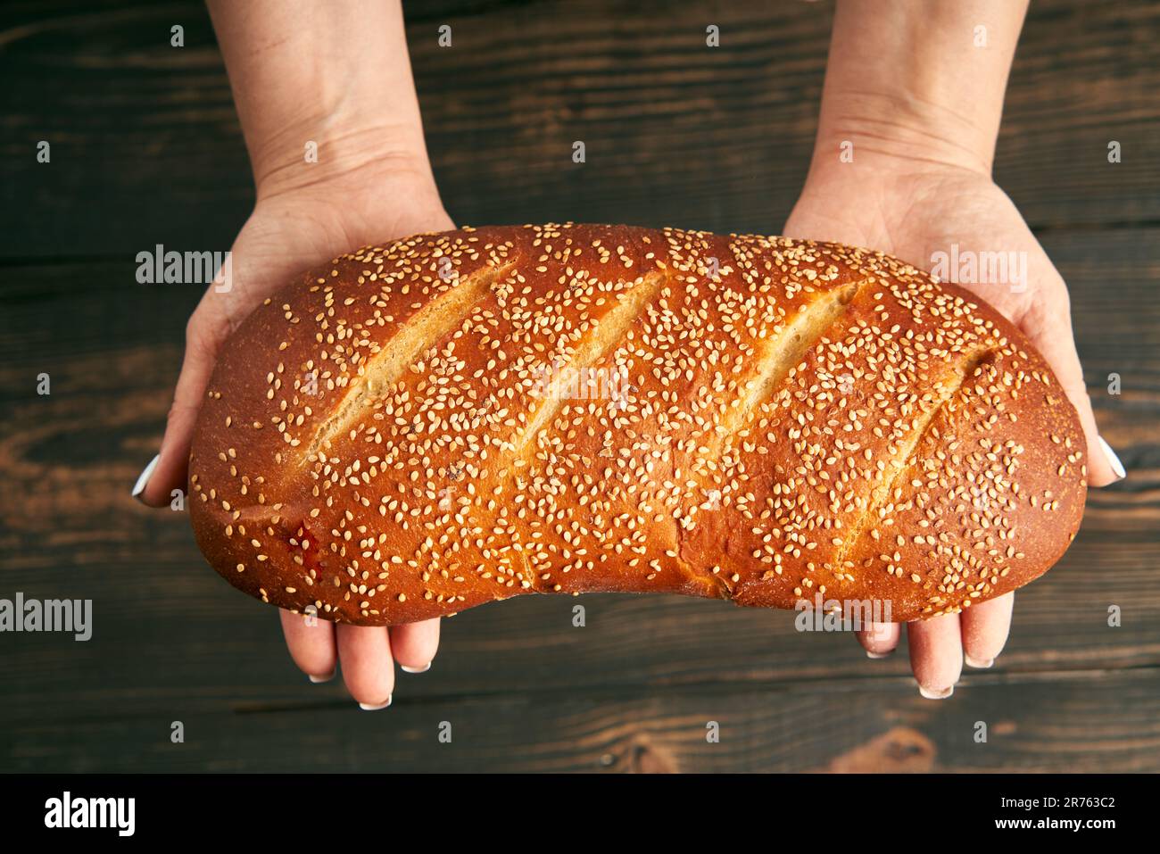 Pagnotta di pane bianco fresco fatto in mani di donna su sfondo tavolo di legno. Panetteria, concetto di cibo Foto Stock