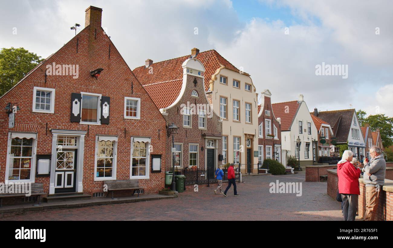 Idilliaco vecchie case a Greetsiel, una piccola pittoresca cittadina di pescatori nel Nord Frisia. Alcuni turisti che camminano poco prima dell'inizio della stagione estiva. Foto Stock
