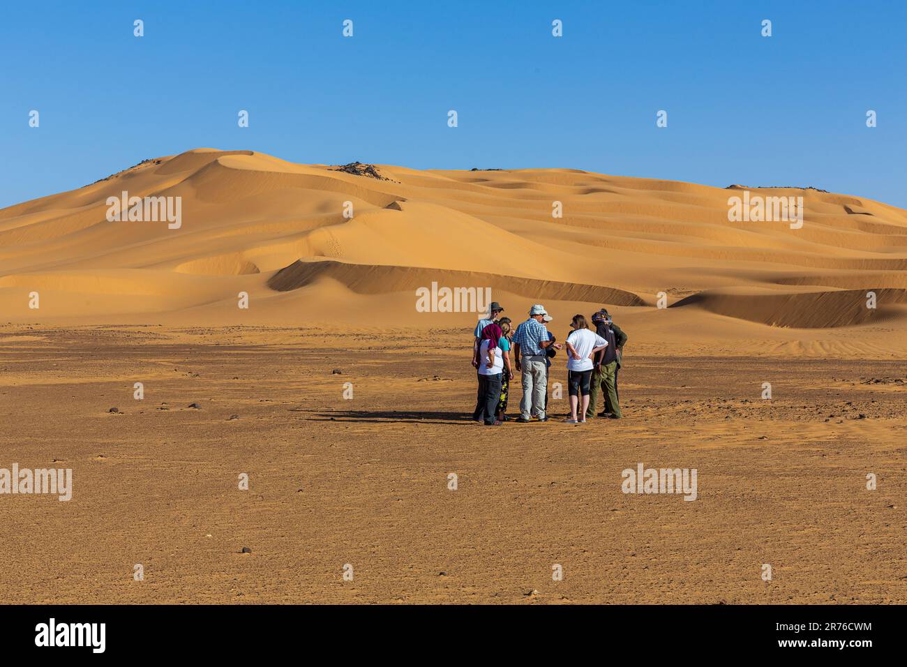 i viaggiatori si riuniscono intorno al tour leader di gruppo sotto il caldo cielo blu del remoto deserto occidentale in sudan per imparare delle attività del giorno Foto Stock