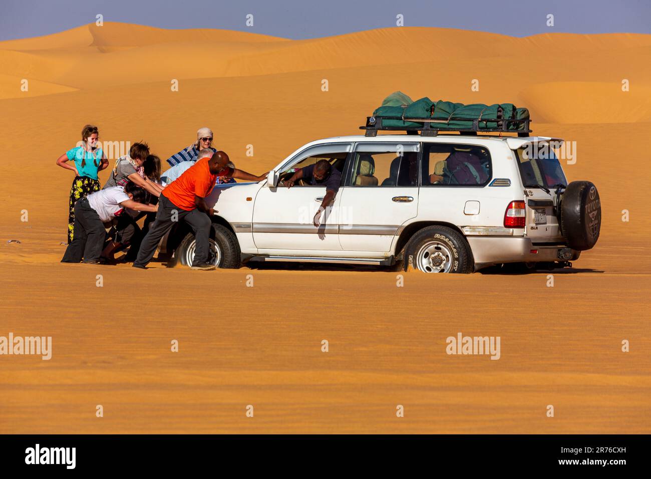 il leader del gruppo dà incoraggiamento mentre il gruppo del tour si unisce a spingere il veicolo a quattro ruote motrici fuori dalla sabbia soffice nel sudan Foto Stock
