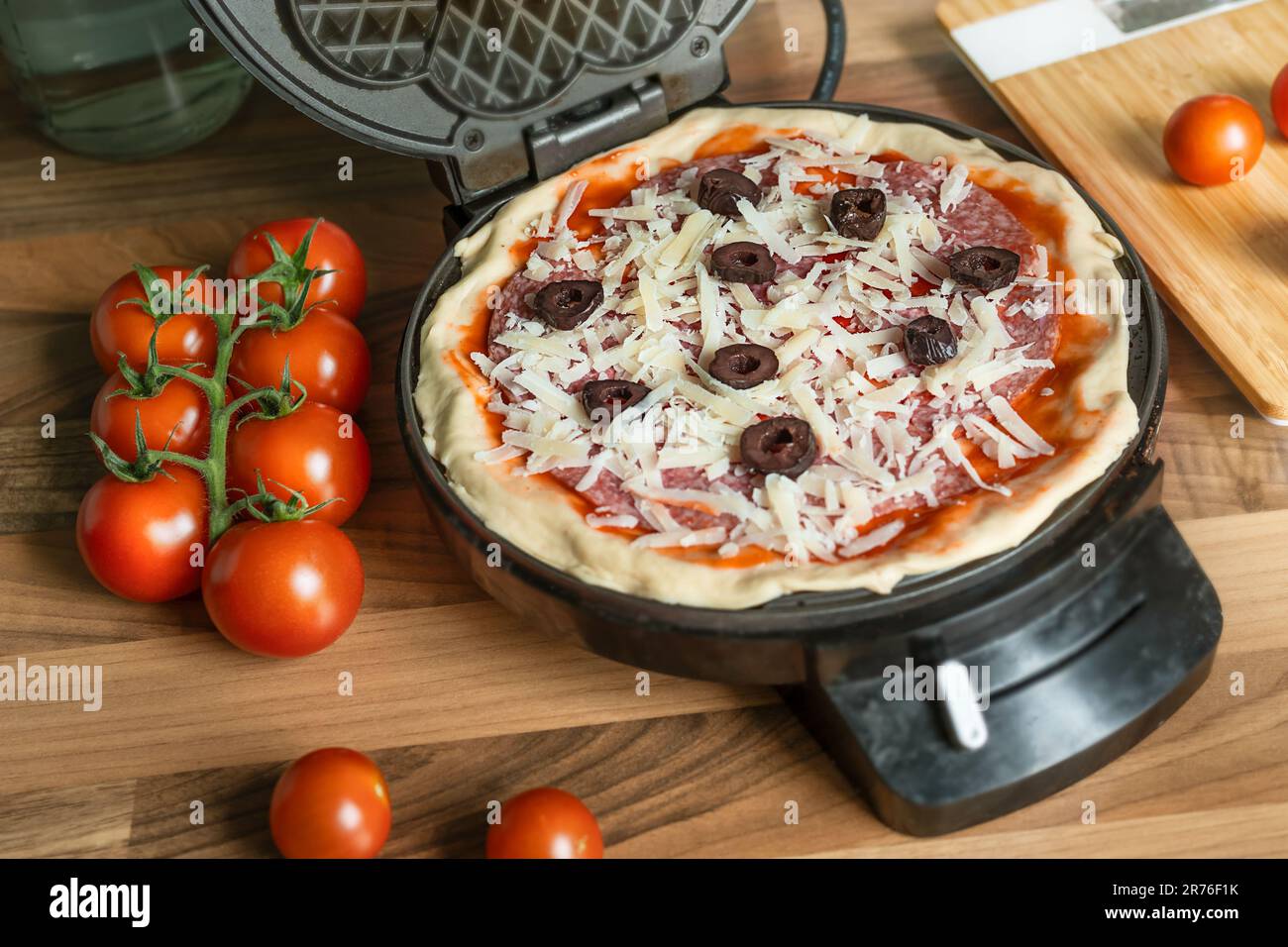 Waffle fatti in casa con peperoni, olive e parmigiano pronti per la cottura in un ferro da stiro Foto Stock