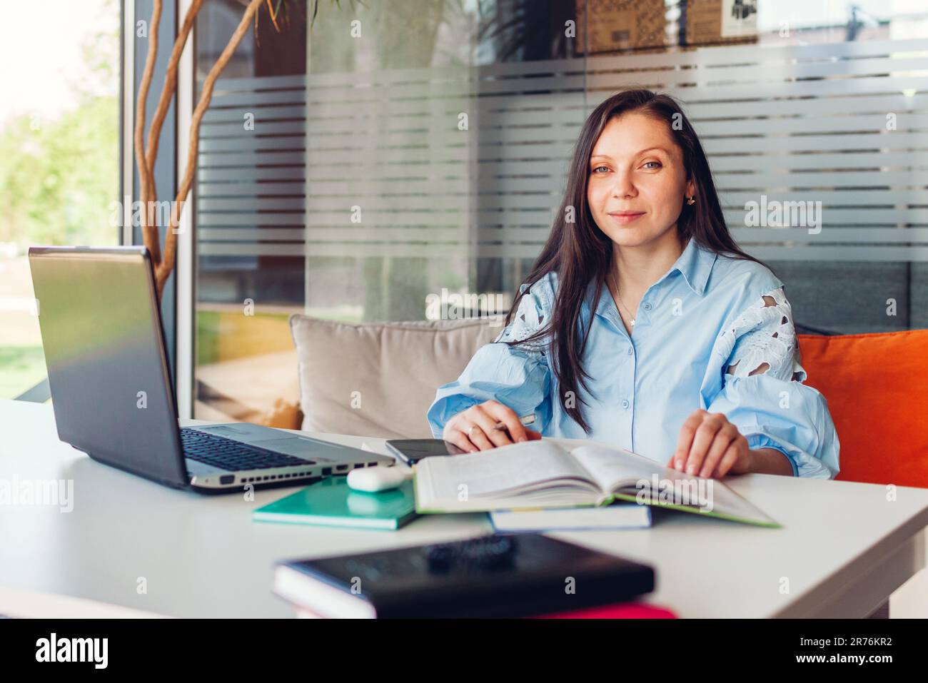 Giovane donna d'affari che lavora online in ufficio utilizzando un notebook. L'insegnante di mezza età guarda la macchina fotografica seduto alla scrivania. Foto Stock