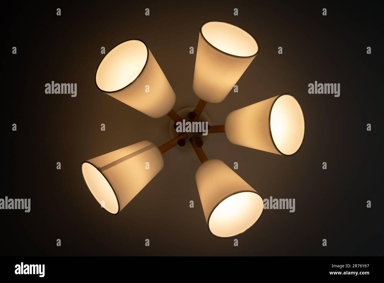 Lampadario moderno con cinque paralumi bianchi che risplendono nel buio, vista dal basso Foto Stock