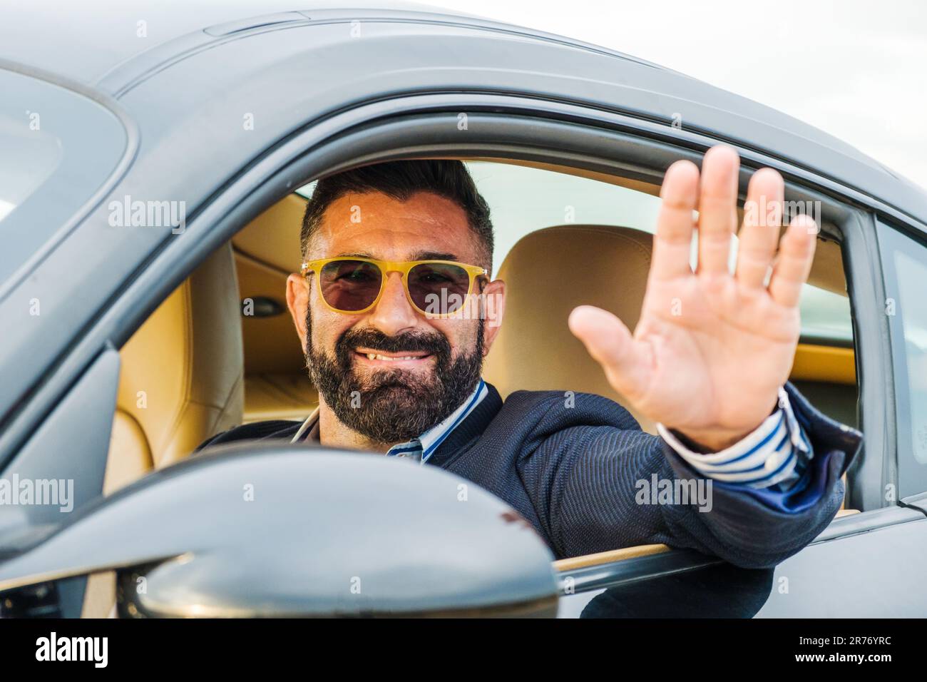 Un giovane uomo sorridente in occhiali da sole ondeggia dalla sua auto Foto Stock